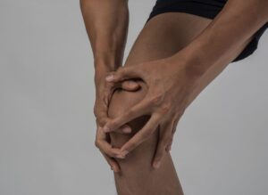 Ein junger Sportler mit kräftigen, athletischen Beinen hält sich nach einer Verletzung am Knie.