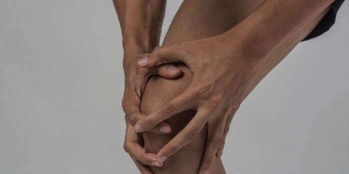 Ein junger Sportler mit kräftigen, athletischen Beinen hält sich nach einer Verletzung am Knie.